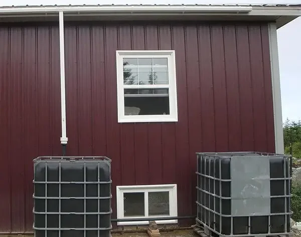 Rainwater collection system with IBC totes beside a red barn