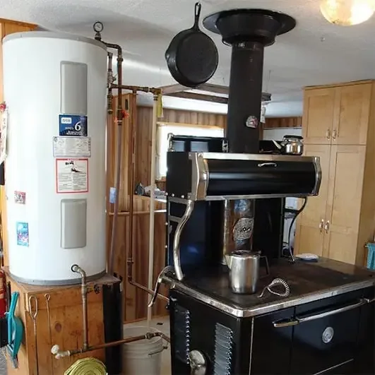 Off-grid kitchen with a black wood cookstove and a water heater